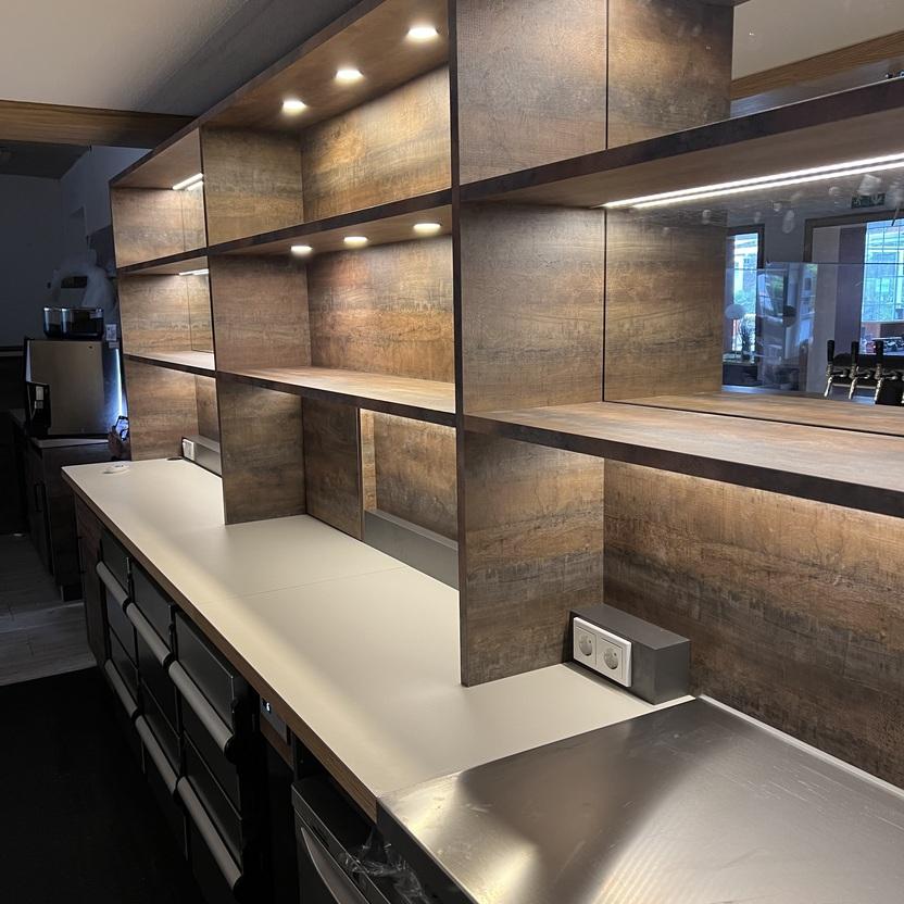 Maßgefertigte Theke mit Beleuchtung von Tischlerei Krogull Hochwertige Theke in Holzoptik mit integrierter LED-Beleuchtung, offenen Regalen und modernen Arbeitsflächen.