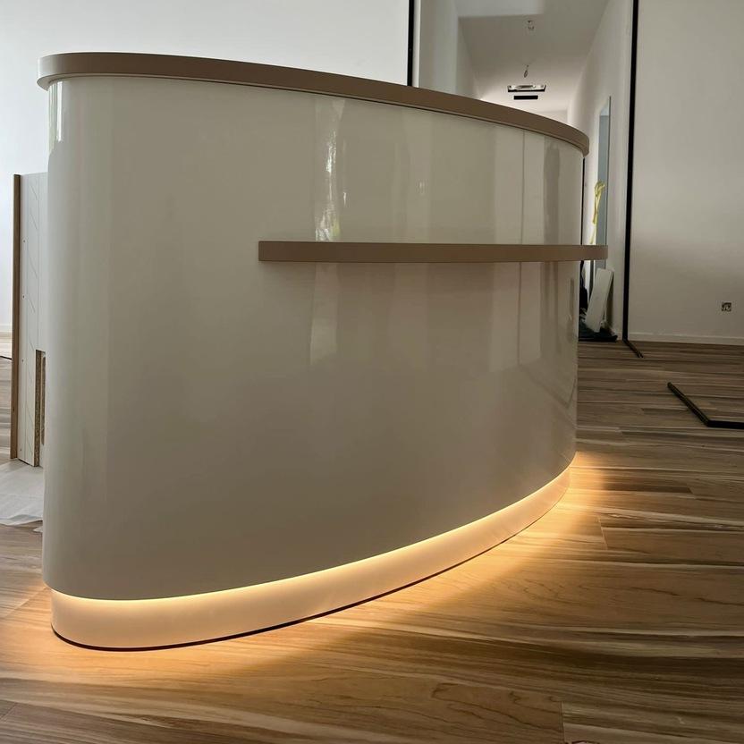 R&uuml;ckseite der runden Theke mit Griffleiste und warmem LED-Sockellicht in hellem Flurraum.