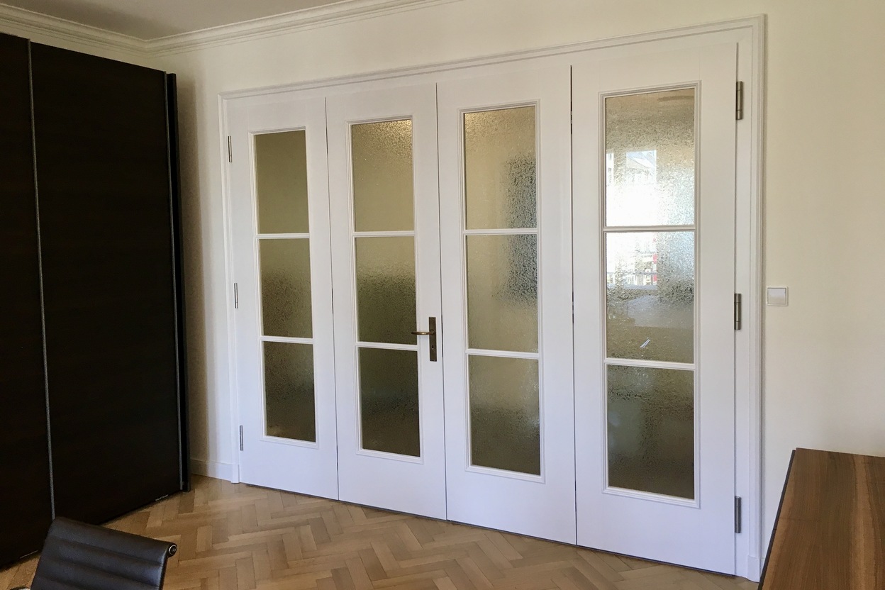 Elegante Glastüranlage mit weißem Holzrahmen und vier Flügeln, die für einen klassischen und lichtdurchfluteten Raum sorgt.